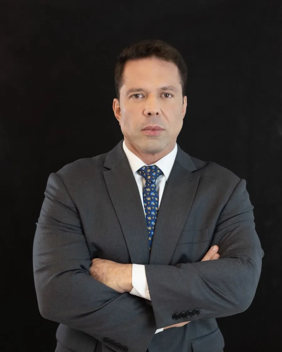 Dr. Fabio Pagnozzi de terno cinza e gravata azul, de braços cruzados, em fundo preto